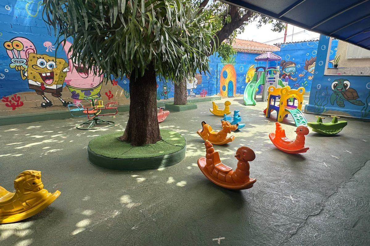 Parquinho coberto da escola, com brinquedos, gangorras e mural colorido